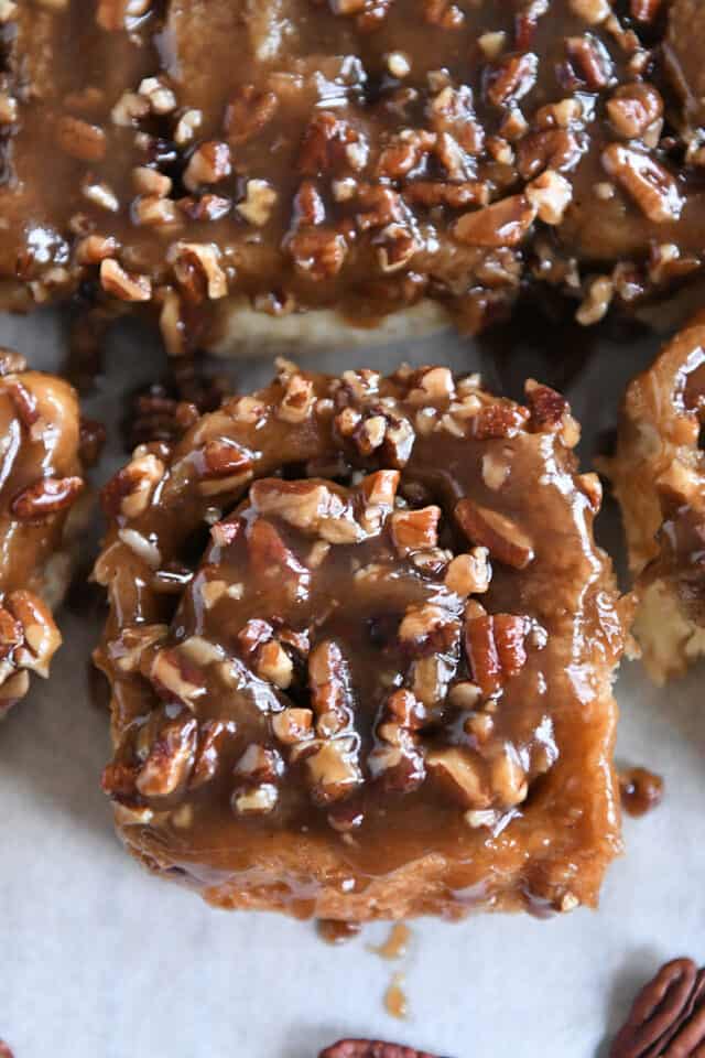 One caramel pecan sticky bun pulled away from full batch on parchment paper.