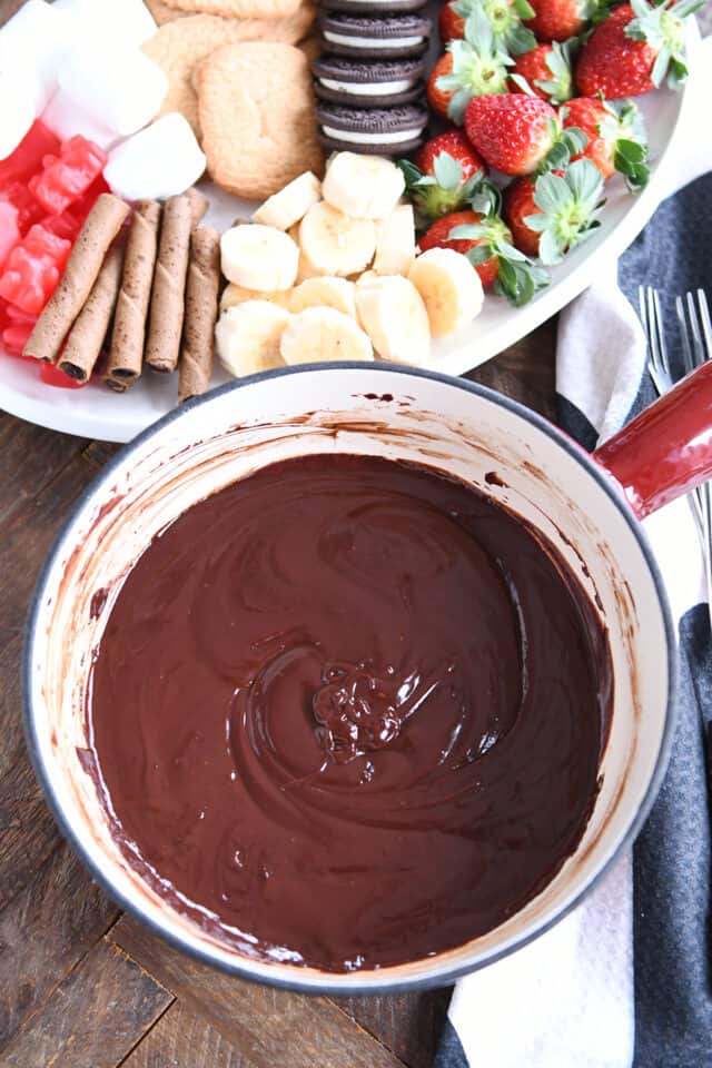 Pot of chocolate fondue with white tray of bananas and strawberries.