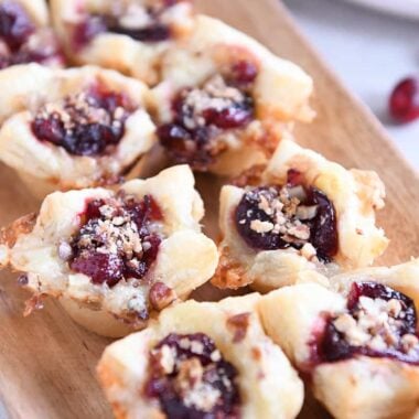 Six cranberry brie bites on wood platter.