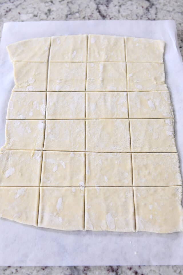 Rolled sheet of puff pastry on parchment paper cut into squares.