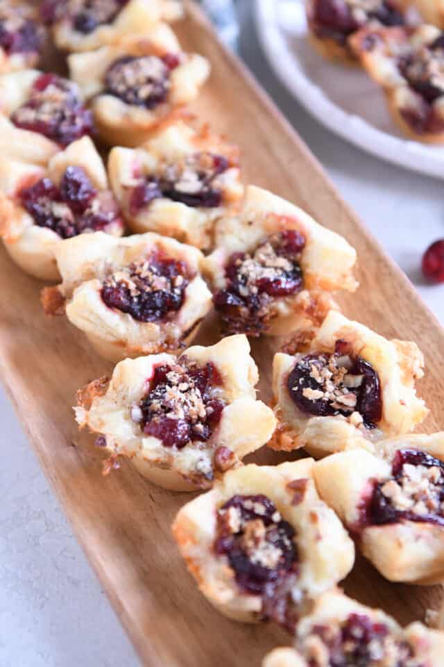 Lots of baked cranberry brie bites on wood platter.
