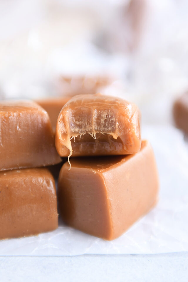 Several gingerbread caramels on white parchment paper with bite out of the top caramel.