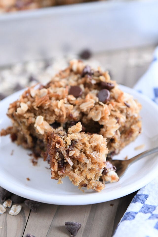 Piece of banana chocolate chip cake on white plate with bite on fork.