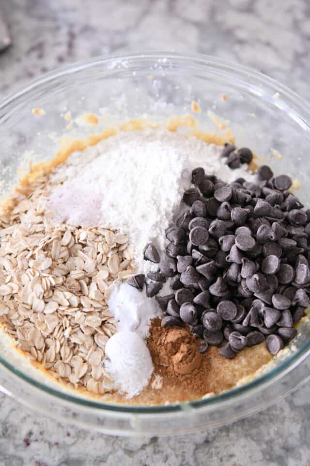 A glass bowl of oats, flour, chocolate chips, cinnamon, salt and banana butter.