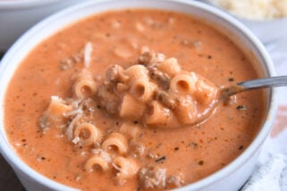 Spoon scooping up bite of soup with tomatoes, noodles, and ground beef.