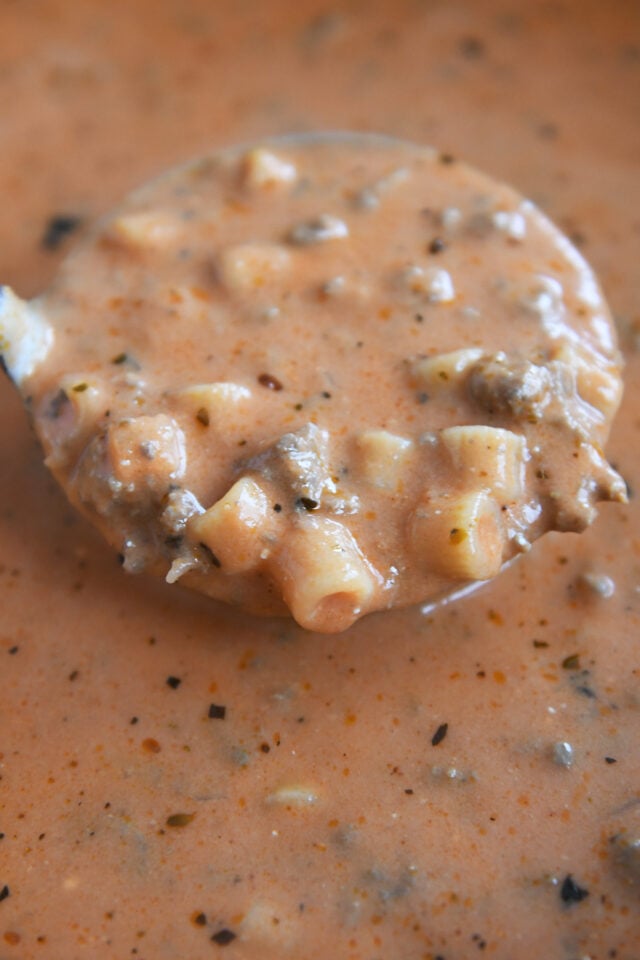 Ladle scooping up soup with noodles, tomatoes and ground beef.