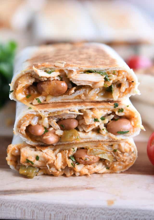 Three tortilla wraps stacked on a wooden board.
