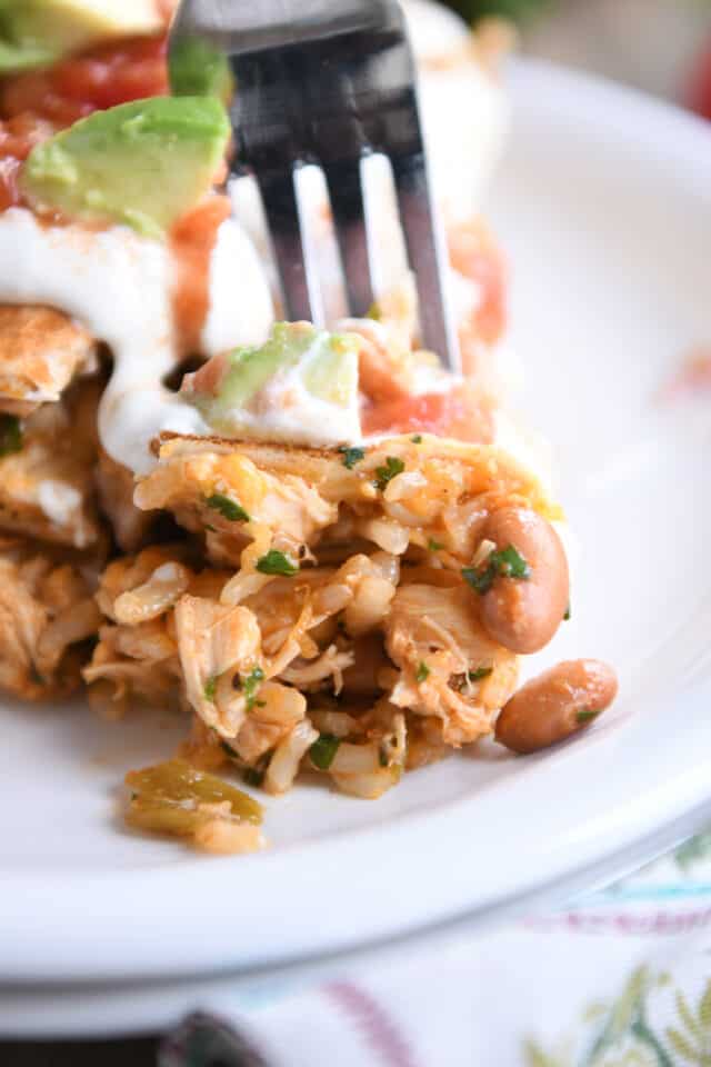 Bite of chicken, rice, and tortilla on fork on white plate.