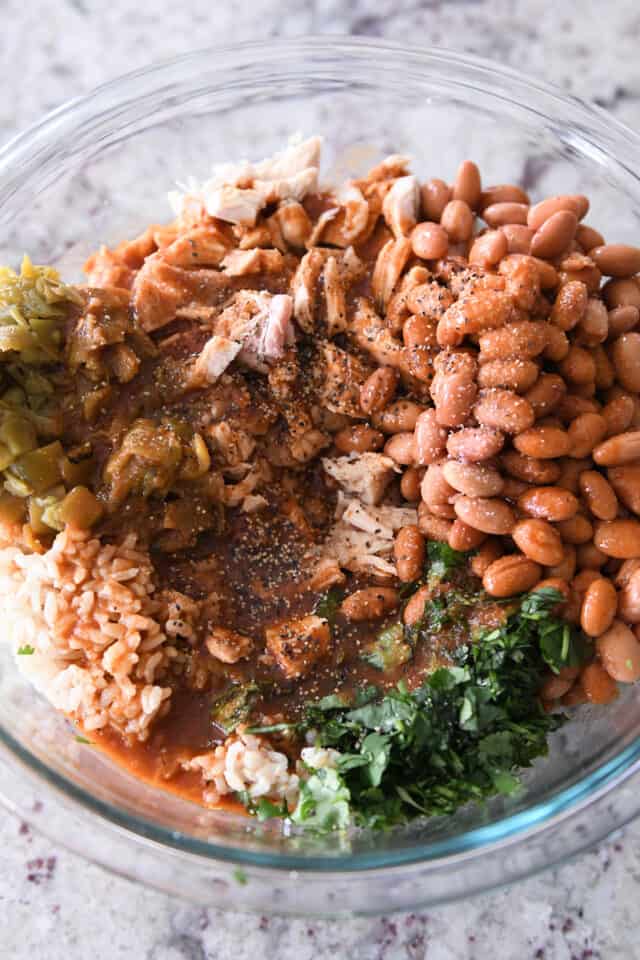 Glass bowl with pinto beans, coriander, brown rice, chicken, green chilies and enchilada sauce.