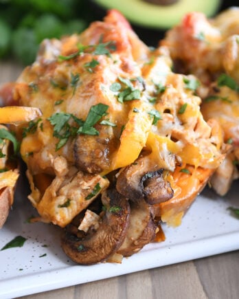 Several sweet potatoes on white tray with mushrooms, bell peppers, and cheese.