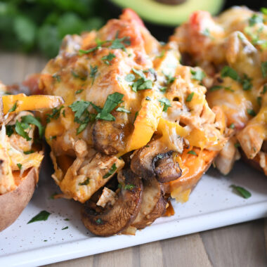 Several sweet potatoes on white tray with mushrooms, bell peppers, and cheese.