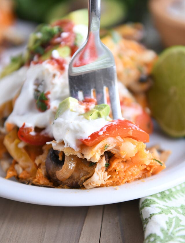 Fork taking bite of sweet potato with bell peppers, mushrooms, sour cream and avocados.