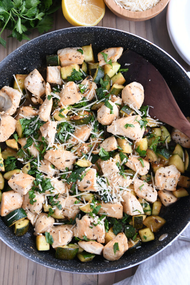 Top down view of nonstick skillet with chicken, zucchini, parsley and parmesan.