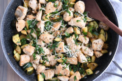 Skillet with chicken, zucchini, parmesan and wooden spoon.