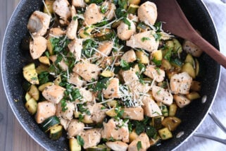 Skillet with chicken, zucchini, parmesan and wooden spoon.