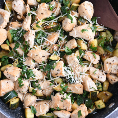 Skillet with chicken, zucchini, parmesan cheese and wooden spoon.
