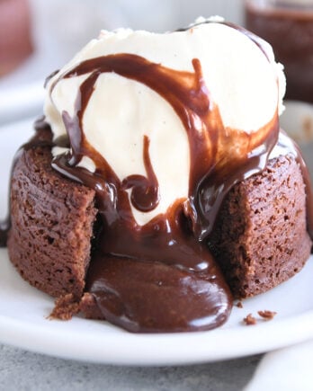 Molten lava cake on white plate with ice cream and spoon.