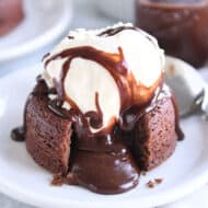 Molten lava cake on white plate with ice cream and fudge sauce.