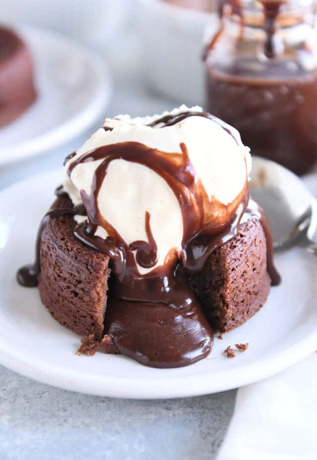 Molten lava cake on white plate with ice cream and fudge sauce.