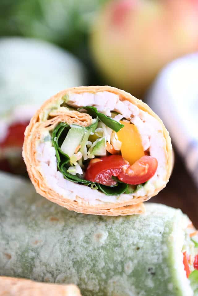 Half of a turkey wrap stuffed with tomatoes, cucumbers, bell peppers and spinach.