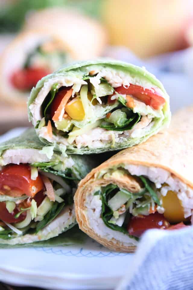 Three turkey avocado veggie wraps on white plate.