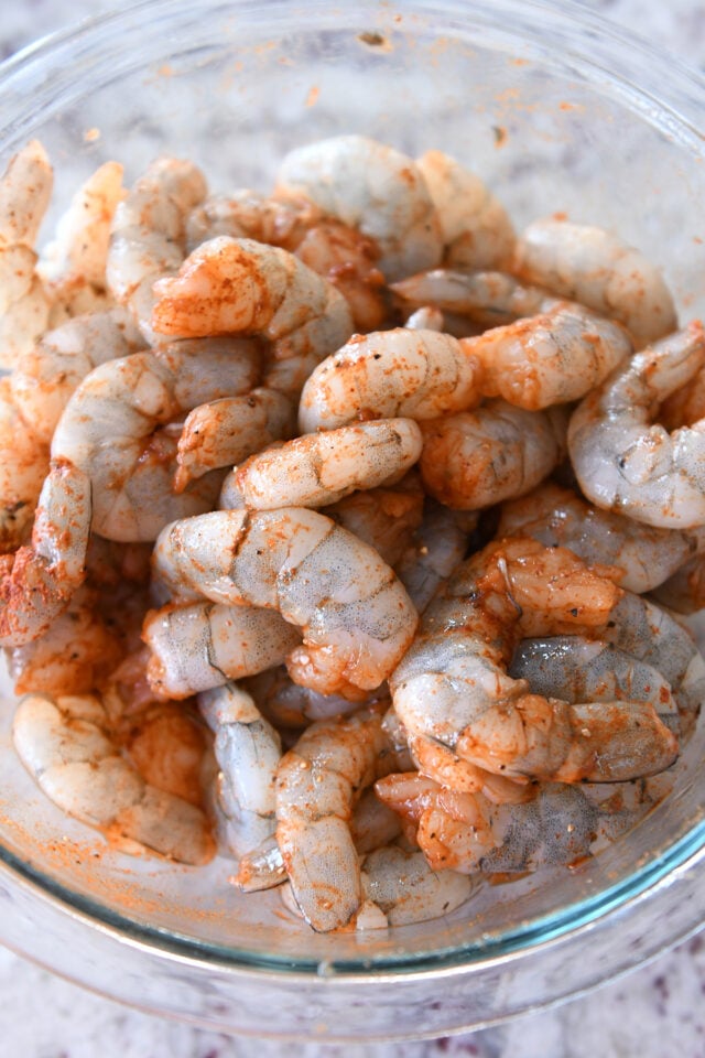 Raw shrimp with paprika in a glass bowl.