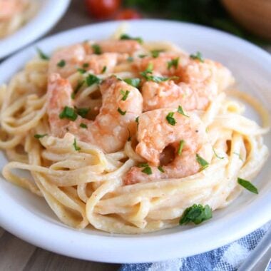 Boiled shrimp on creamy linguine on white plate.