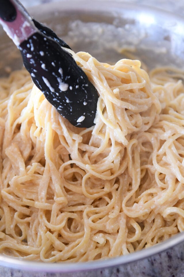 Using tongs to toss pasta in cream sauce.