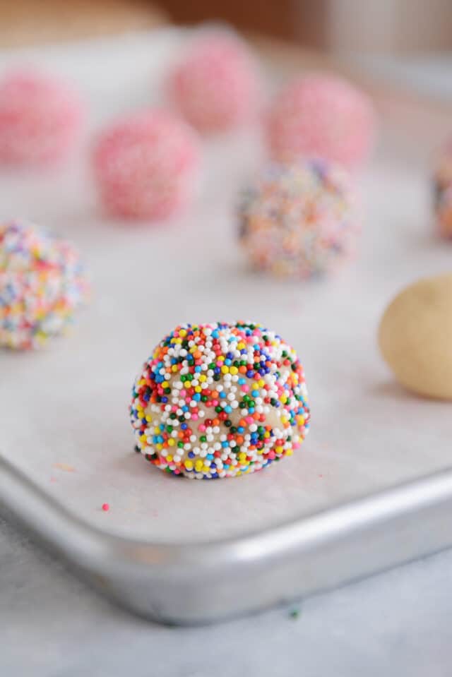 Cookie dough ball rolled in sprinkles on sheet pan.