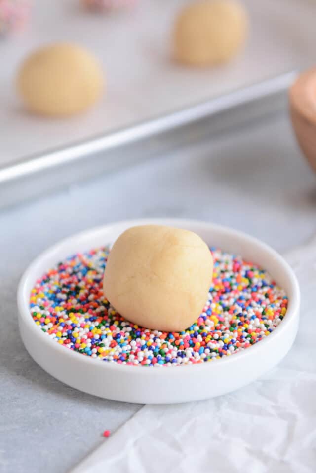 Sugar cookie dough ball sitting in tray of sprinkles.