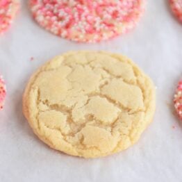 Baked sugar cookie on sheet pan next to cookies with sprinkles.