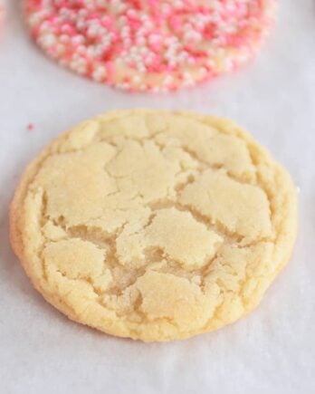 Baked sugar cookie on sheet pan next to cookies with sprinkles.