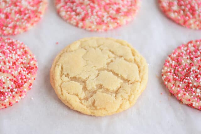 Baked sugar cookie on sheet pan next to cookies with sprinkles.