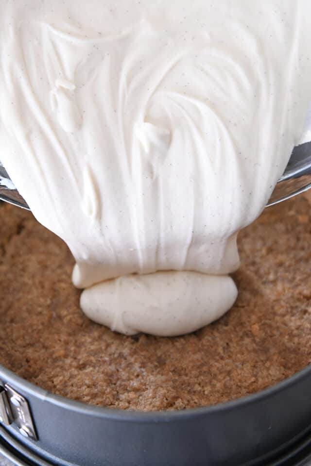 Pouring cheesecake batter onto graham cracker crust.