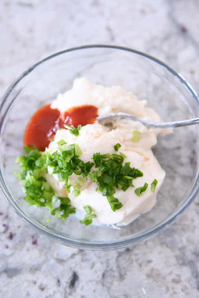 Glass bowl with mayo, sour cream, green onions and sriracha.