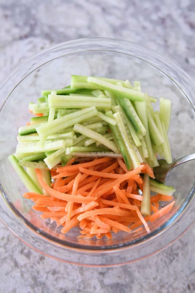 Glass bowl with shredded carrots and cucumbers.