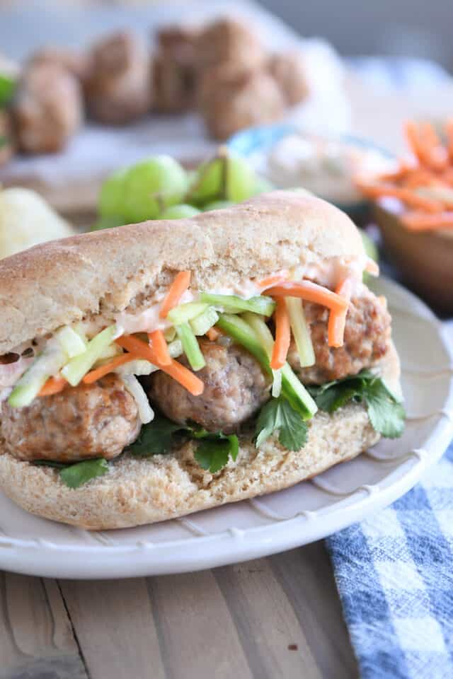 Assembled banh mi meatball sub on cream striped plate.