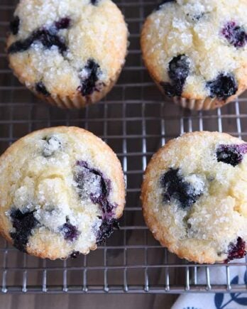 Three baked blueberry muffins on wire cooling rack.