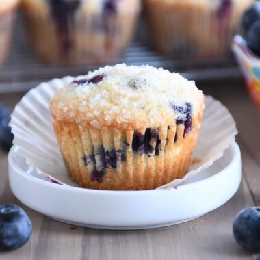 Baked blueberry muffin with paper liner on small white dish.