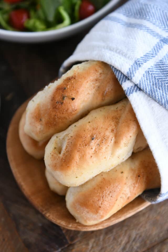 Buttered breadsticks in towel on wood board.