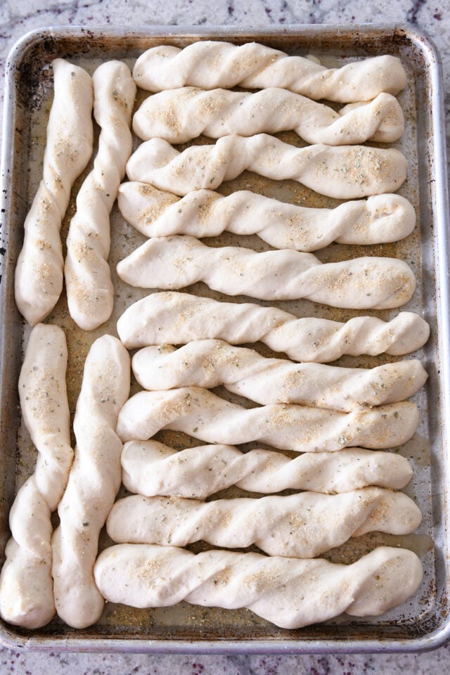 Risen breadsticks on buttered half sheet pan.