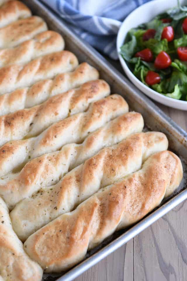 Baked pan of breadsticks with salad in background.