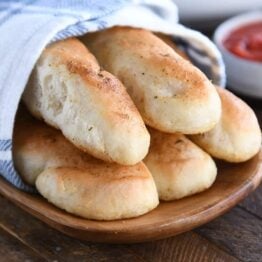 Five breadsticks on wood board with marinara sauce.