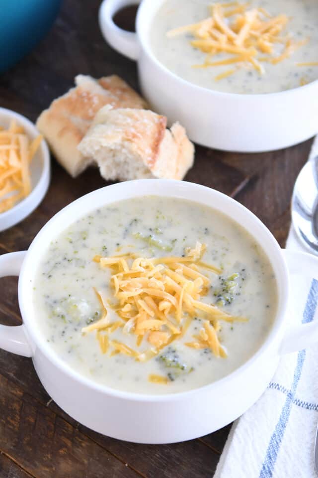 Broccoli cheese soup in white bowls with shredded cheddar.