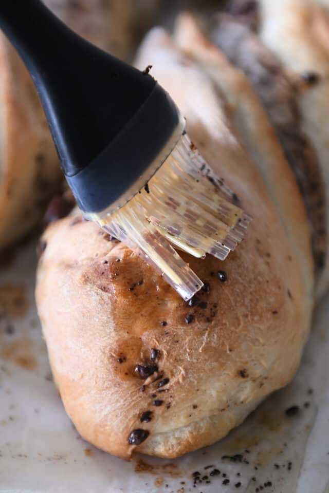 Brushing butter over baked loaves of French bread.