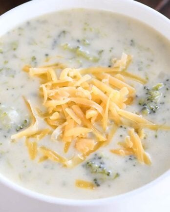 Broccoli cheese soup in white bowl with cheddar cheese.