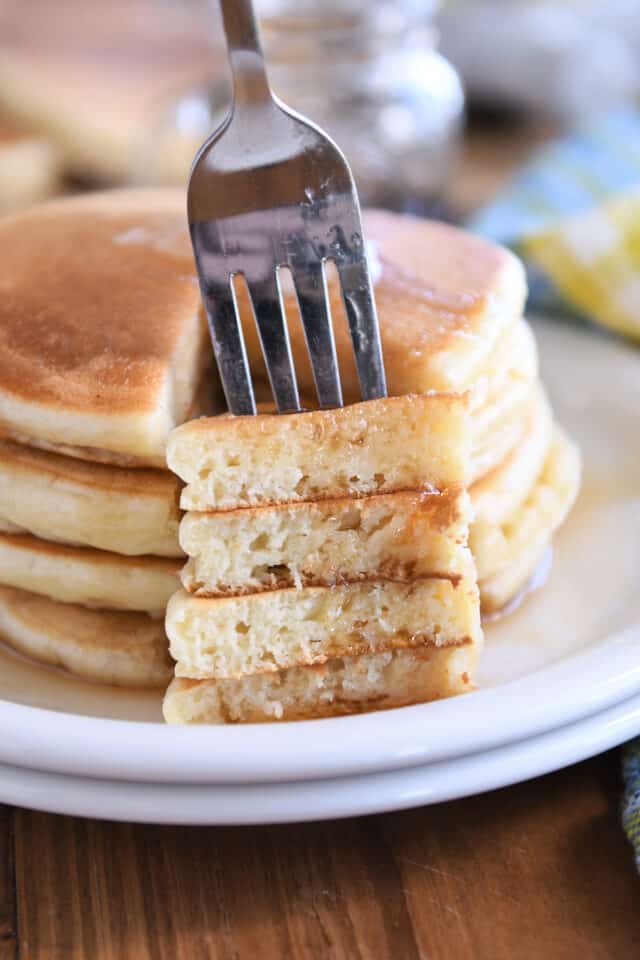 Fork spearing bite of four stacked pancakes.