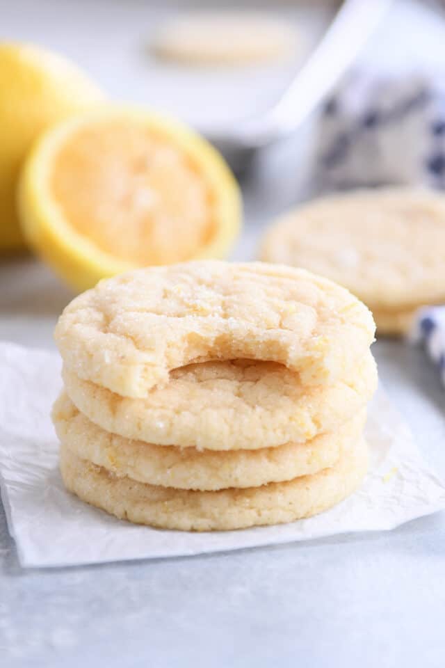Three stacked lemon sugar cookies with one on top with bite taken out.