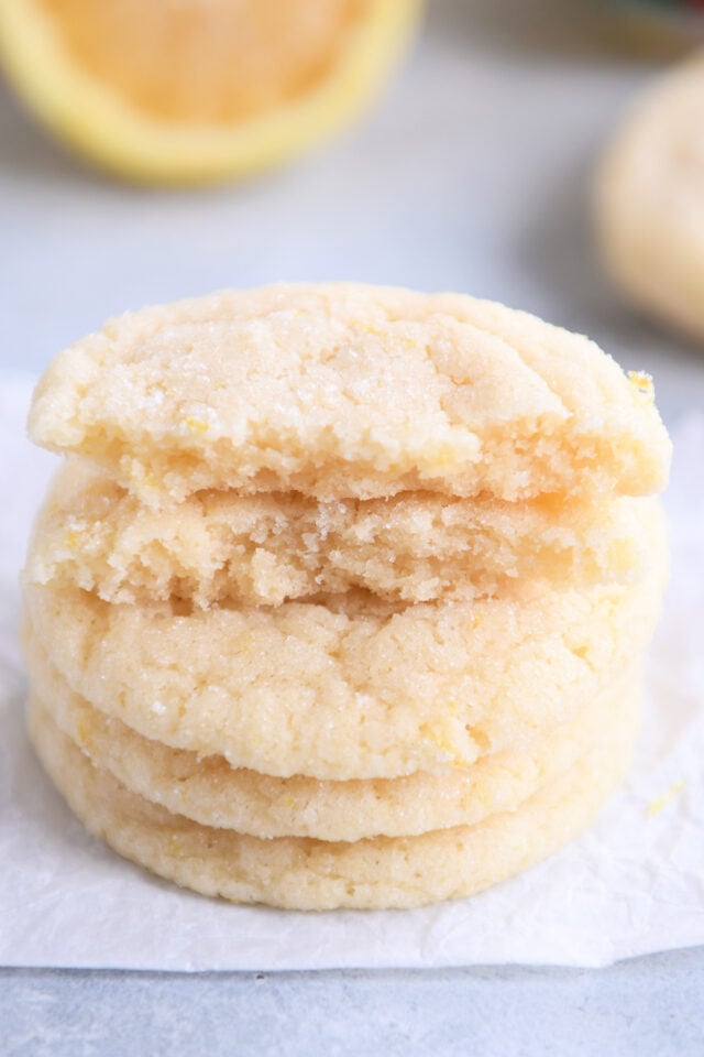Close up of two broken cookie halves on top of a stack of lemon sugar cookies.