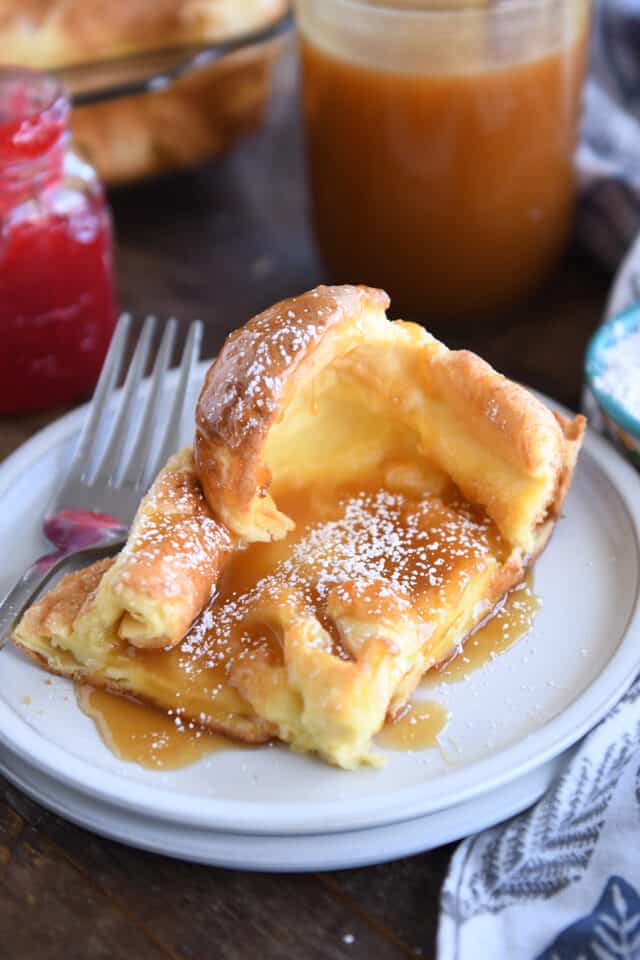 Square of baked German pancake on white plate with powdered sugar and syrup.